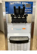 Inox lágyfagylaltgép kék háttéren Softpro 2300 felirattal, fekete adagolókarokkal